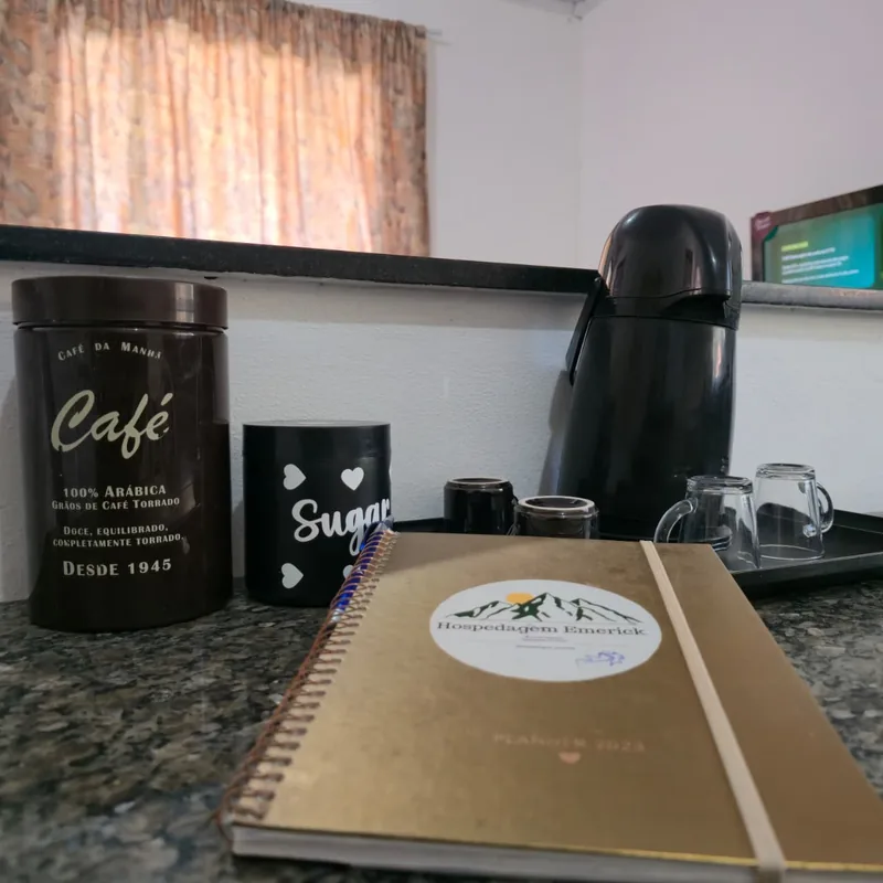 Bandeja de café da manhã com garrafa térmica, xícaras, potes de café e açúcar sobre a bancada de granito, ao lado do planner da hospedagem.