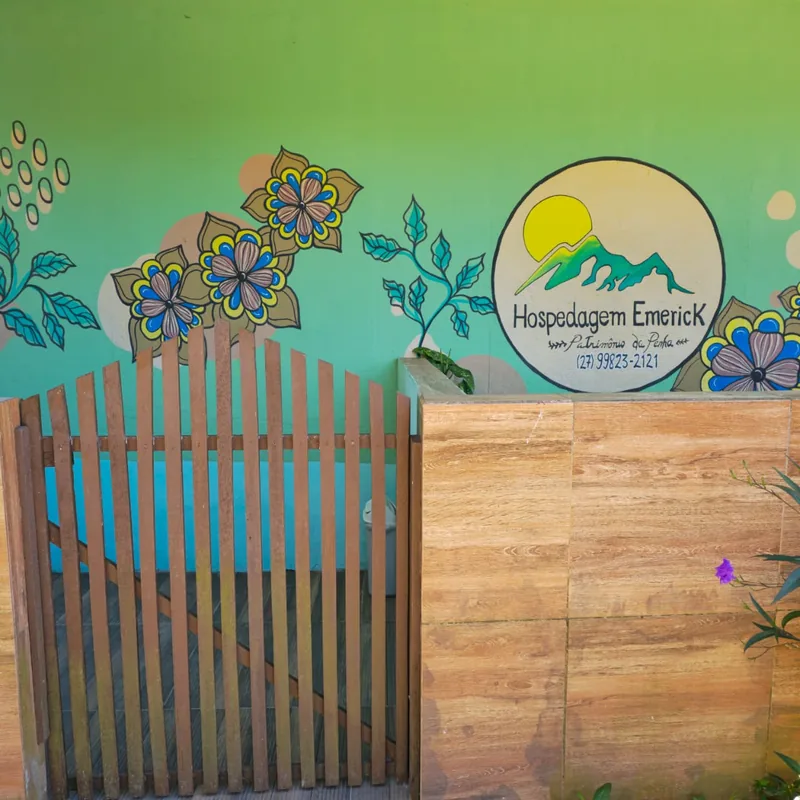 Fachada com mural verde pintado à mão, flores estilizadas e o logotipo do sol e das montanhas.