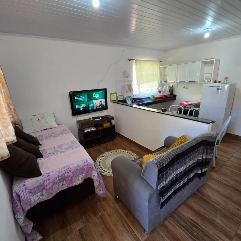 Sala de estar integrada à cozinha, com sofá, cama de apoio, TV e bancada, num apartamento tipo estúdio.